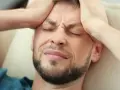 Mężczyzna z bólem głowy trzyma ręce na skroniach, z zamkniętymi oczami i grymasem na twarzy.
