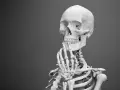 Model ludzkiego szkieletu z ręką przy podbródku, na szarym tle.