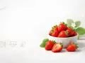 Miseczka pełna świeżych truskawek z listkami i jedną przekrojoną na pół.