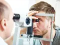 Okulista wykonuje badanie dna oka młodemu mężczyźnie za pomocą specjalistycznego sprzętu.