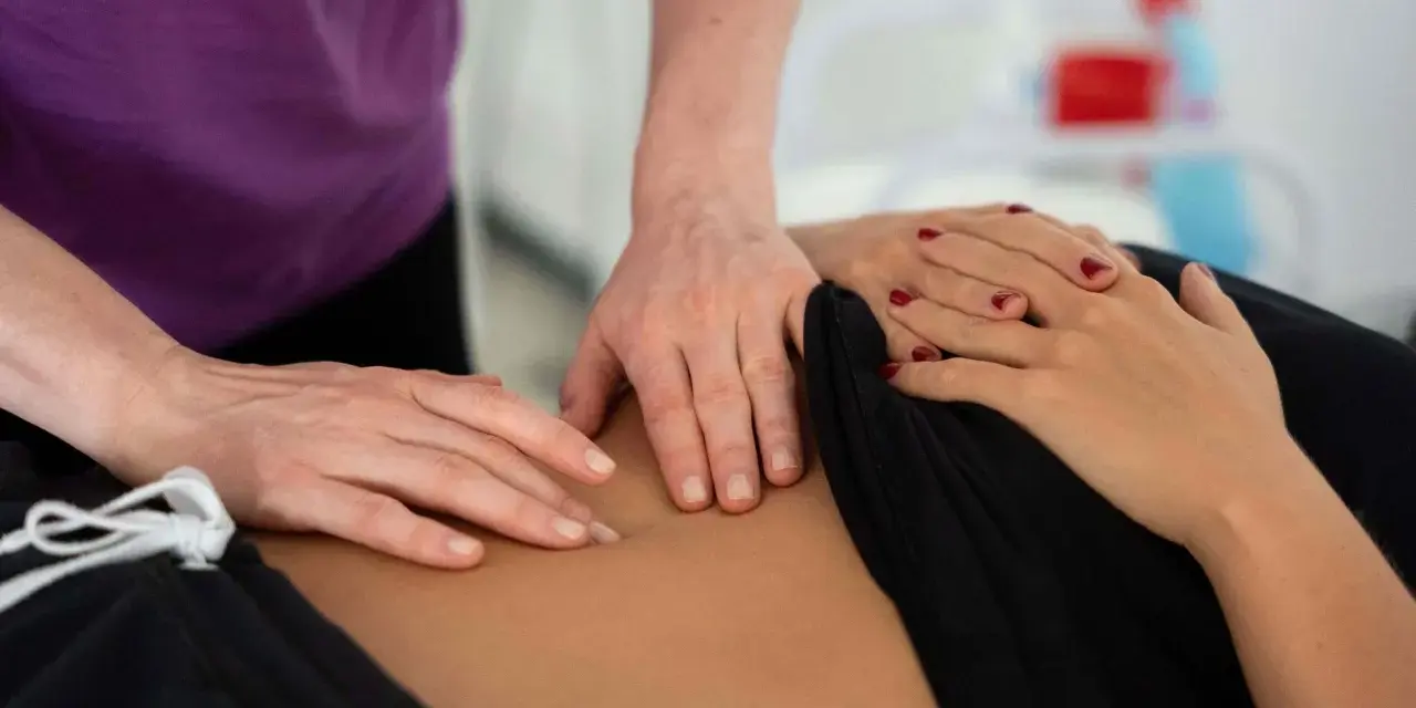 Dłonie terapeuty wykonujące masaż brzucha pacjentki.