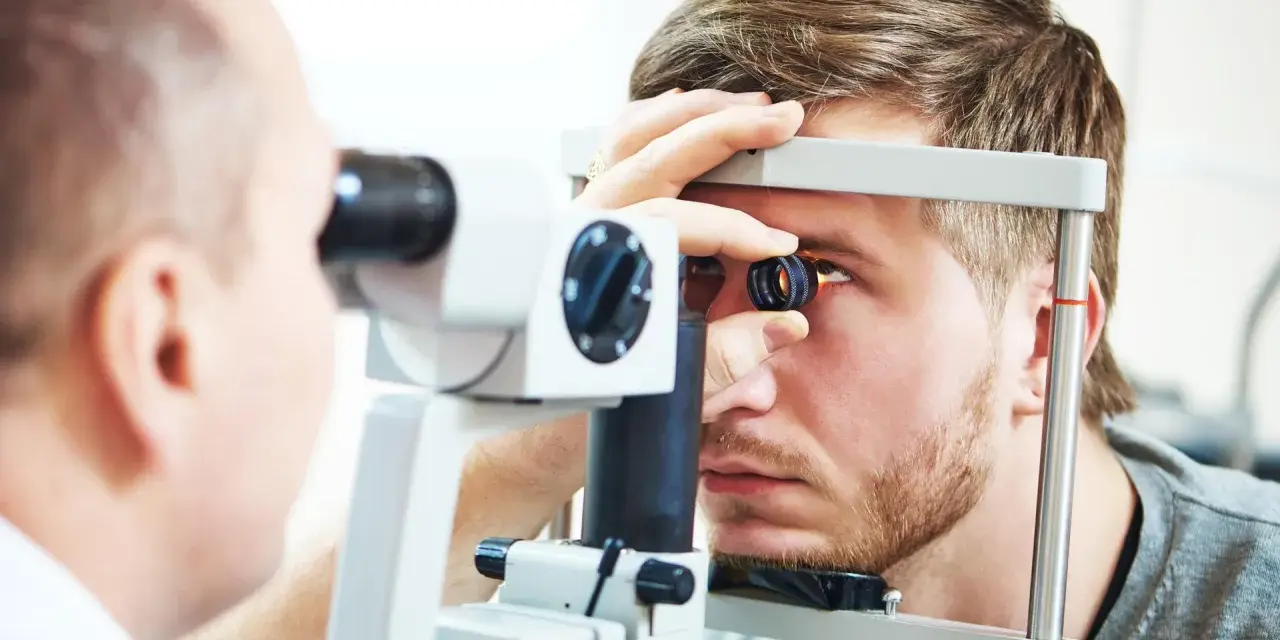 Okulista wykonuje badanie dna oka młodemu mężczyźnie za pomocą specjalistycznego sprzętu.