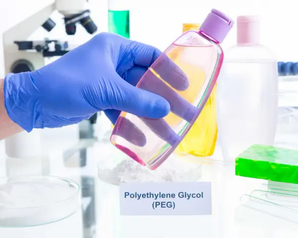 Ręka w niebieskiej rękawiczce trzyma buteleczkę z różowym płynem, w tle laboratorium i kosmetyki.
