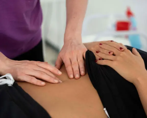 Dłonie terapeuty wykonujące masaż brzucha pacjentki.