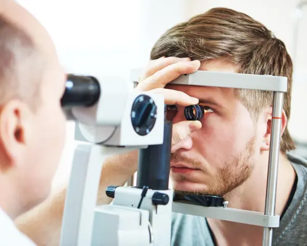 Okulista wykonuje badanie dna oka młodemu mężczyźnie za pomocą specjalistycznego sprzętu.