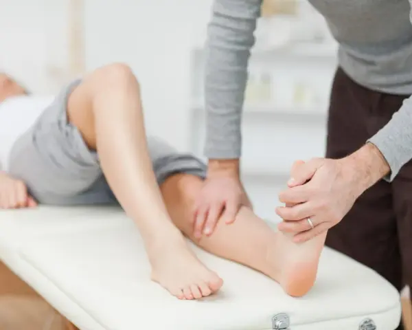 Fizjoterapeuta bada nogę pacjentki leżącej na kozetce.