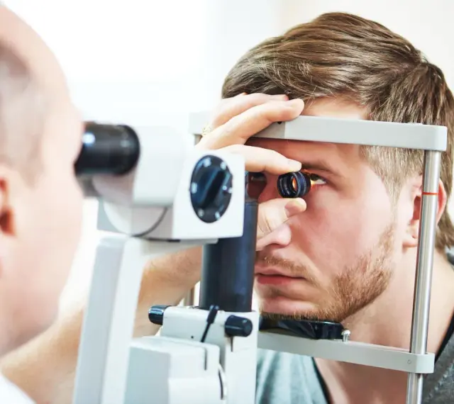 Okulista wykonuje badanie dna oka młodemu mężczyźnie za pomocą specjalistycznego sprzętu.